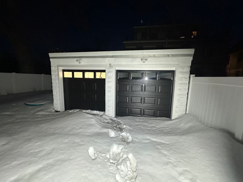Black dual garage doors with windows on detached garage at night in deep snow — MA